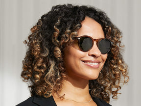 Model is wearing The MILTZEN SUN in Tobacco in size 49 with Calibar Green Lenses