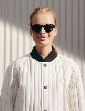 Model is wearing The GRUNYA SUN in Antique Tortoise in size 47 with G-15 Glass Lenses